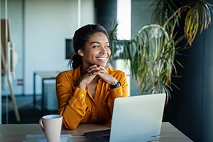 Woman in orange shirt smiling while sitting at desk in office