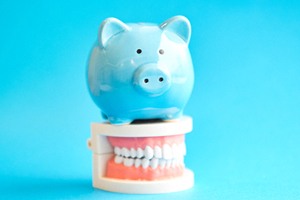 Piggy bank atop model teeth representing cost of dental implants in Ontario
