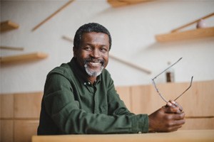 Smiling man sitting at desk and holding his glasses