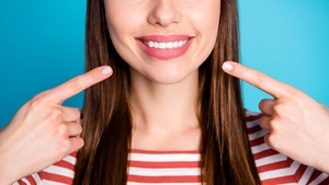 An image of a woman pointing to her new smile that is complete with veneers in M5R 3K4