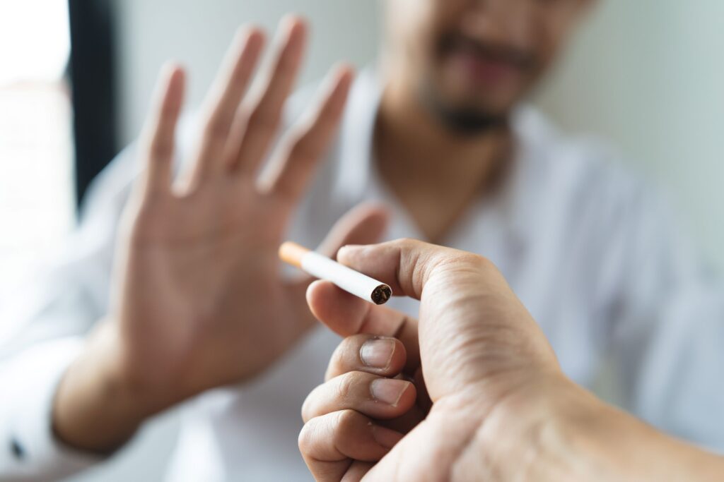 Man blurry in background holding palm out to turn down offered cigarette